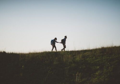 couple walking on hill while holding during daytime