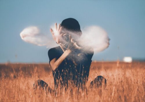 man sitting on brown grass field playing with smoke